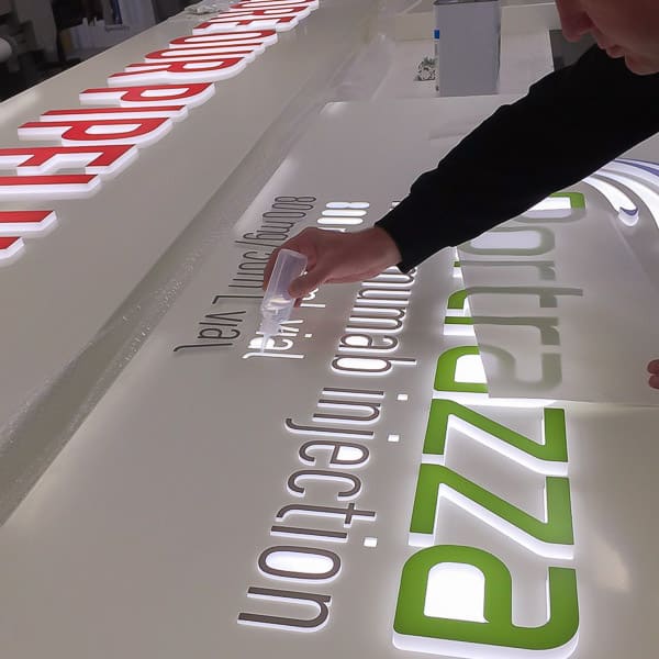 Acrylic letters with vinyl faces being glued into a routed aluminium tray with opal acrylic diffuser