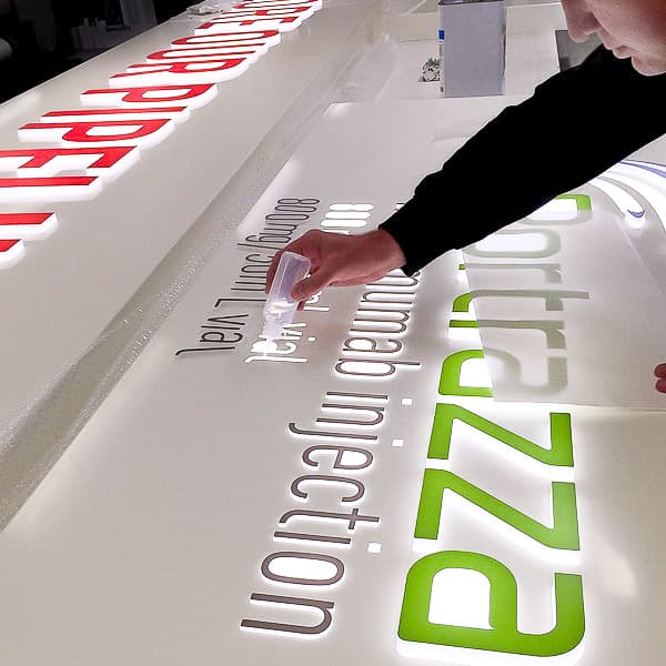 Acrylic letters with vinyl faces being glued into a routed aluminium tray with opal acrylic diffuser