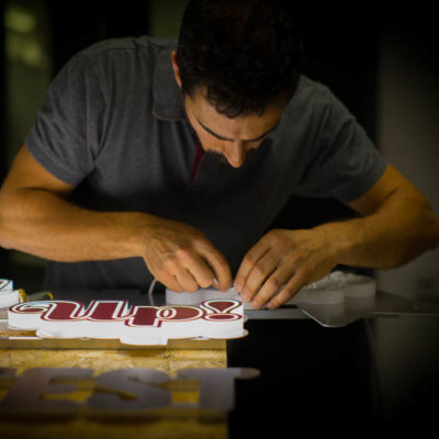 An illuminated sign in construction with skilled engineer fitting LED's into place